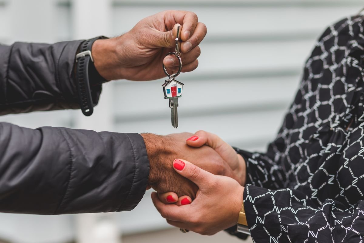 One person handing a set of house keys to another outside a home, the closing moment when a home sale's capital gain gets measured