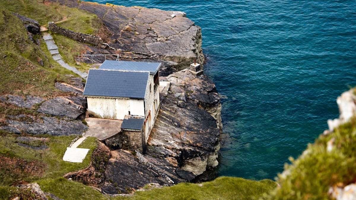 A weathered house perched on an exposed rocky coastal cliff above the ocean