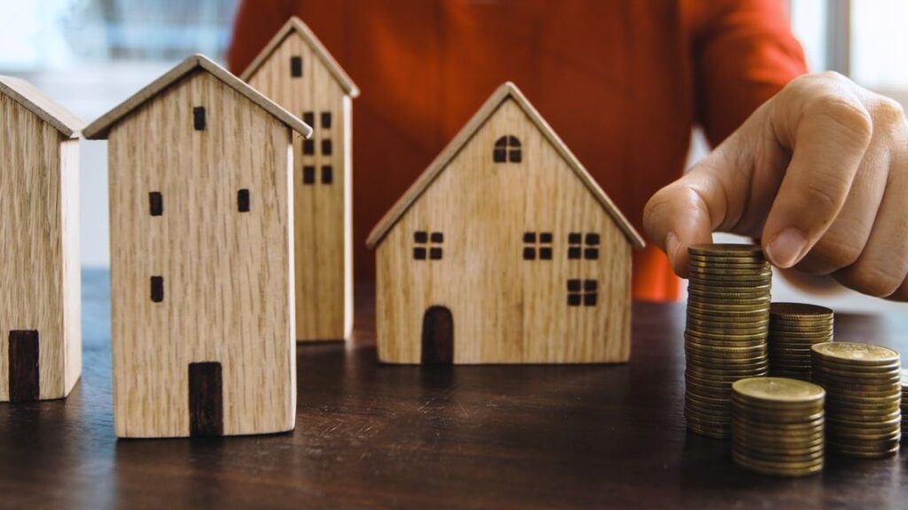 Wooden model houses beside stacks of coins, illustrating how a DSCR loan qualifies a rental property's cash flow instead of your paycheck