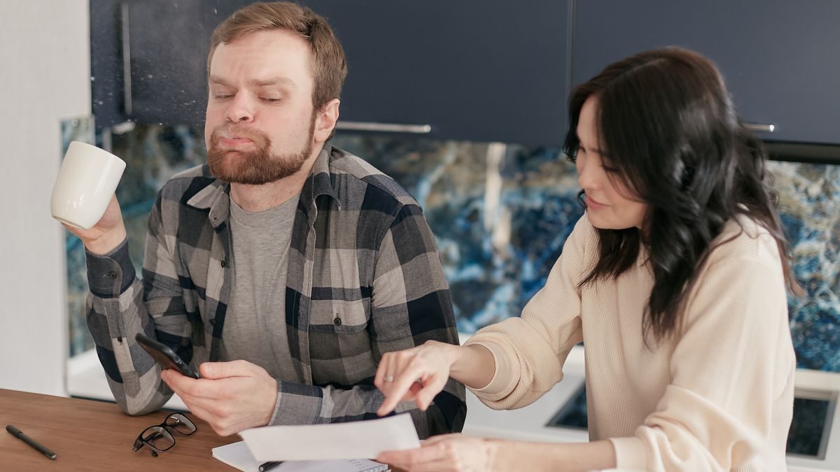 A couple at their kitchen table reviewing a home insurance renewal bill with concern